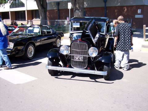 1972 Ford Ranchero - A black vintage car is displayed with its hood open, parked next to a black Pontiac Firebird.