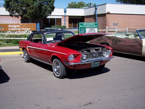 1972 Ford Ranchero - Red 1967 Ford Mustang coupe with hood open, parked on asphalt near a school.