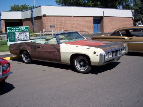 1972 Ford Ranchero - This convertible shows significant body damage and mismatched paint, parked in front of a school.