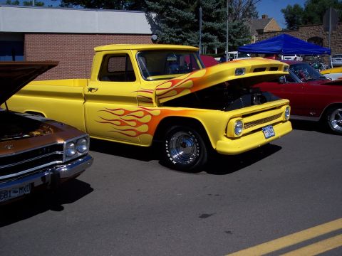 1972 Ford Ranchero - A bright yellow pickup truck with custom flame graphics and its hood open is displayed at an outdoor event.