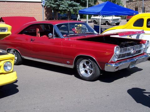 1972 Ford Ranchero - A red 1966 Ford Fairlane coupe is displayed with its hood open, revealing the engine bay. The vehicle is parked outdoors with other cars ne…