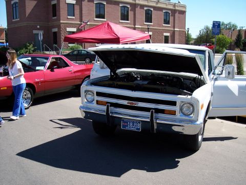 1972 Ford Ranchero - A white 1971 Chevrolet pickup truck is displayed with its hood open, parked next to a red car.