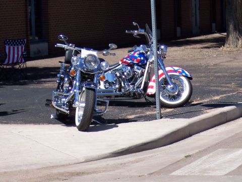 1972 Ford Ranchero - Two motorcycles, one with a prominent American flag paint scheme, are parked side-by-side on a paved area next to a sidewalk.