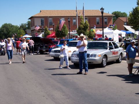1972 Ford Ranchero - A silver police car is parked on a street during an outdoor event with several other vehicles and people.