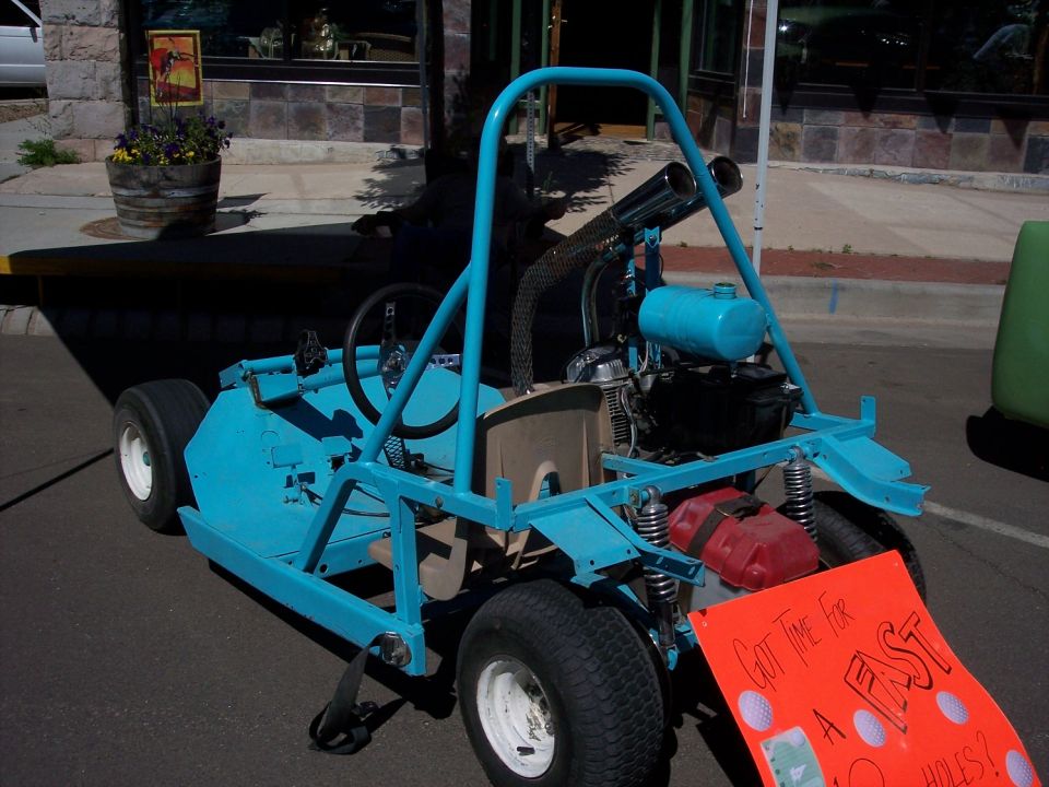 Blue go-kart with roll cage, dual exhaust, and a red gas can, parked on asphalt