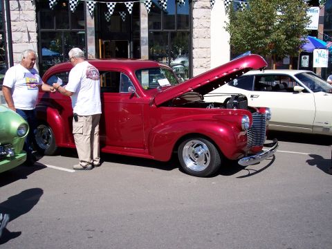 1972 Ford Ranchero - Two men converse next to a shiny red classic car with its hood raised at an outdoor event.