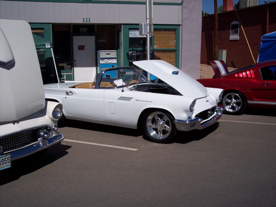 White 1955 Ford Thunderbird convertible with hood open, parked next to a red car