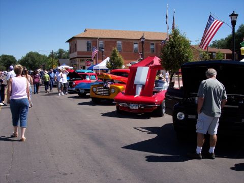 1972 Ford Ranchero - A street filled with classic cars, including a red 1963 Chevrolet Corvette Stingray, on a sunny day.