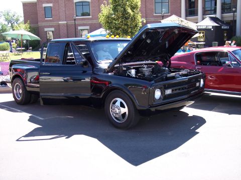 1972 Ford Ranchero - A black dually pickup truck is parked with its hood open, next to a red vehicle, under a sunny sky.