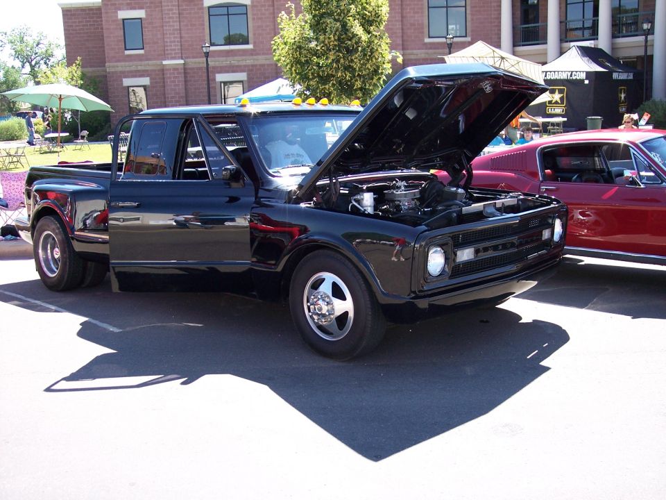 Black dually pickup truck with hood open, parked next to a red car. The truck has a custom grille and dual rear wheels