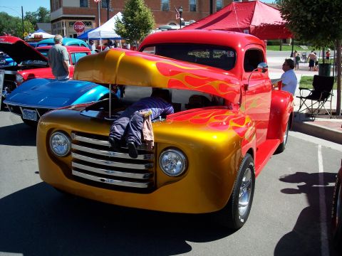 1972 Ford Ranchero - A person works on the engine of a brightly colored pickup truck at an outdoor event.
