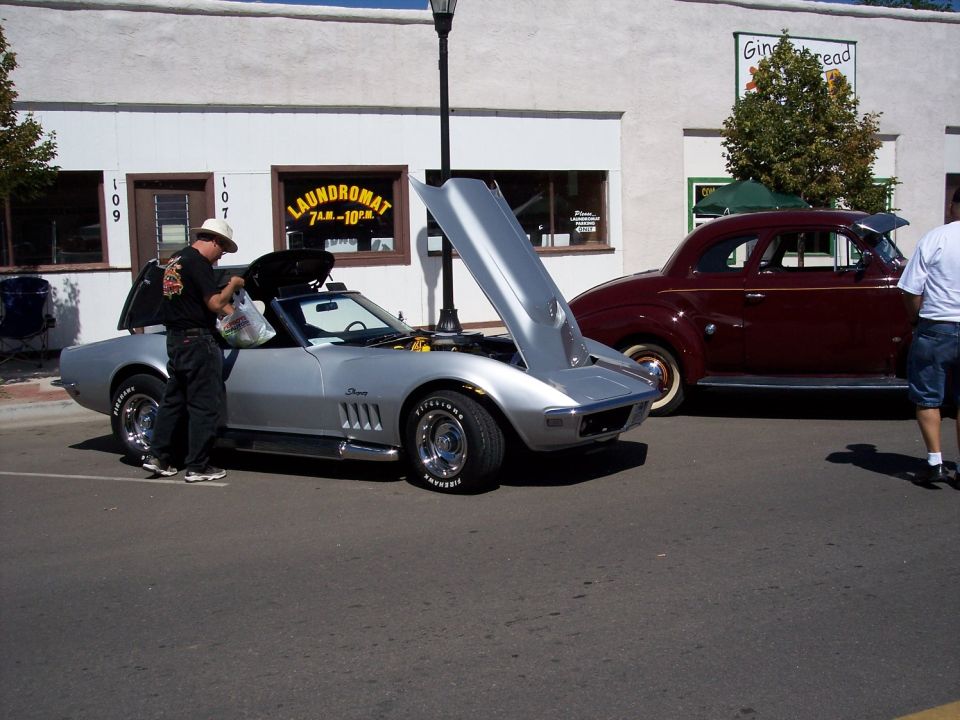 Silver convertible sports car with hood open, man loading items into trunk