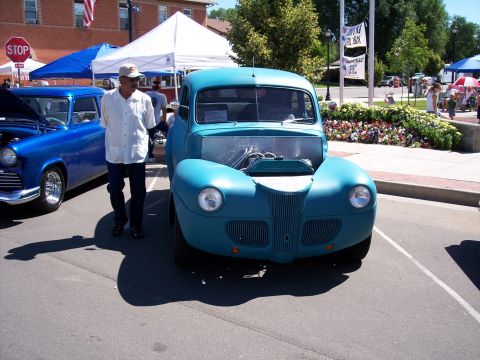 1972 Ford Ranchero - A man stands by a teal hot rod truck with its hood open at an outdoor car show.