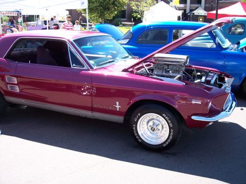 1972 Ford Ranchero - A custom Ford Mustang with a prominent engine is parked next to a blue sedan at an outdoor event.