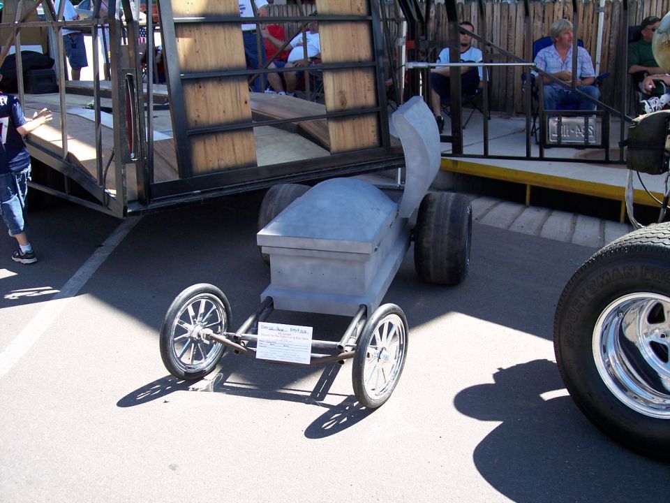 coffin car with small front wheels and large rear wheels, next to a trailer