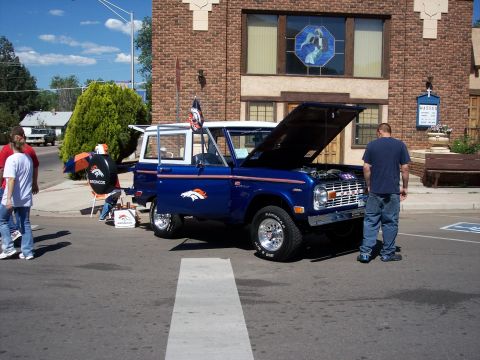 1972 Ford Ranchero - A blue Ford Bronco with the hood up and doors open is parked on a street in front of a brick building.