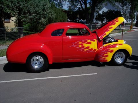 1972 Ford Ranchero - A vibrant red hot rod with custom yellow flame graphics is displayed with its hood open, revealing the engine.