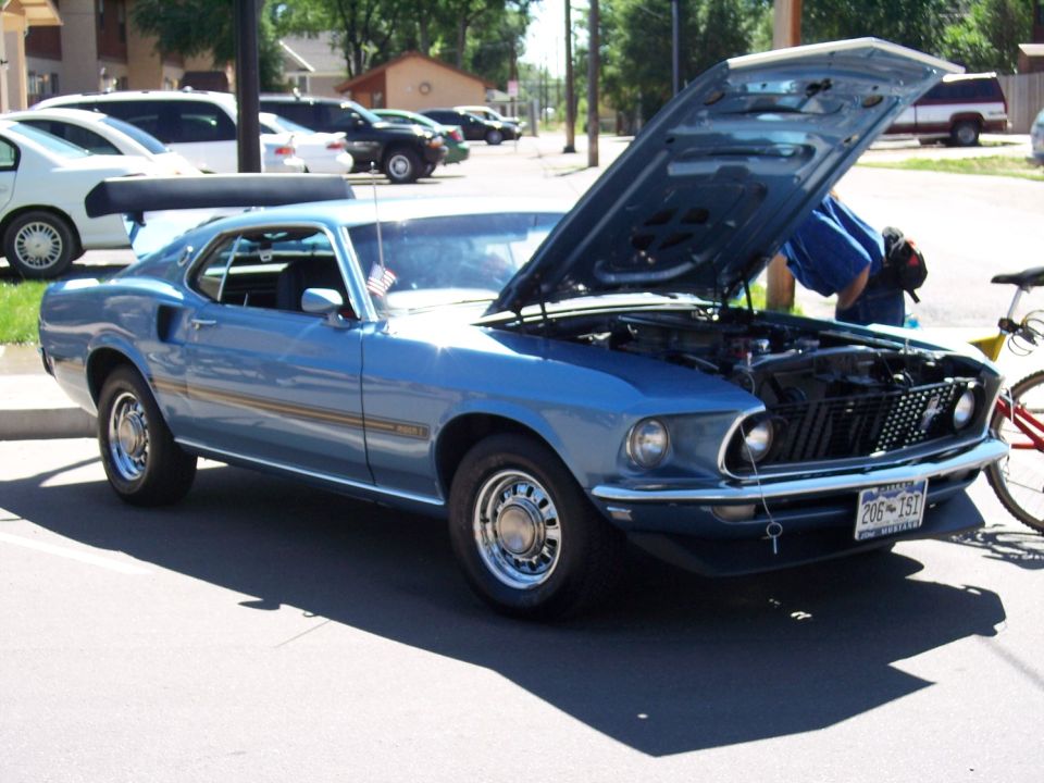 Blue 1969 Ford Mustang Mach 1 with hood open, showing engine and front grille. License plate reads 206-TST