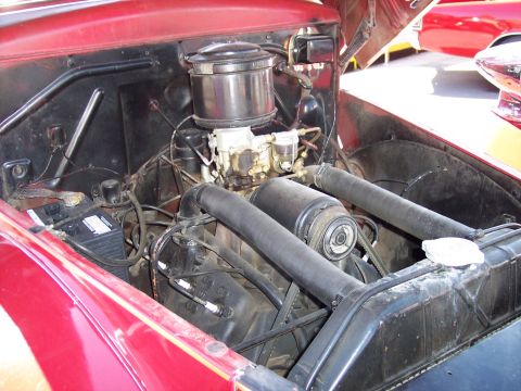 1972 Ford Ranchero - The engine bay of a red vehicle, showing its V8 engine and components, with another vehicle in the background.