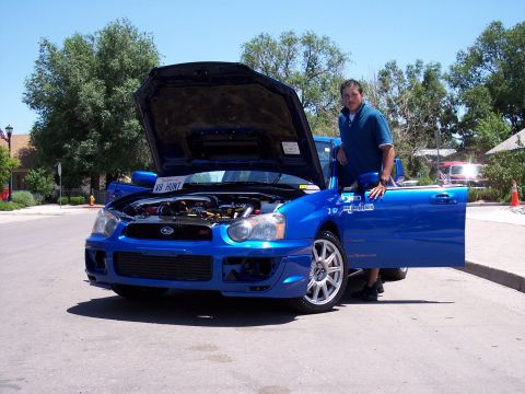 1972 Ford Ranchero - A man stands next to a blue Subaru Impreza WRX with its hood and driver's door open.
