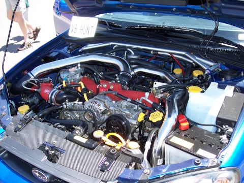 1972 Ford Ranchero - The engine bay of a blue Subaru is displayed, with a sign indicating "V8 HUNT".