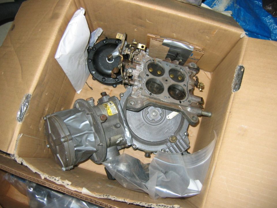 Cardboard box with a carburetor and fuel pump inside. Some plastic bags and paper are also visible