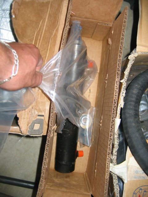 1992 Ford Mustang - A person's hand is shown holding a plastic-wrapped power steering pump within a cardboard box.