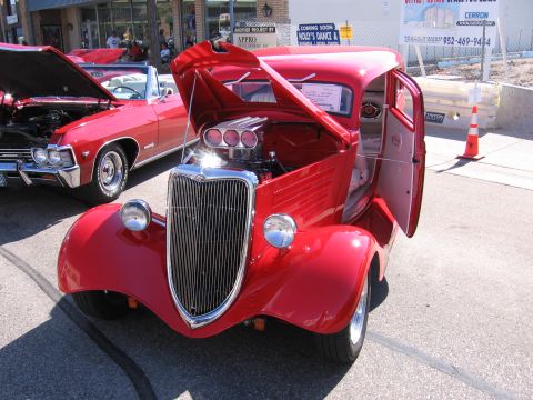 1989 Ford Mustang - A red hot rod is displayed with its hood and door open, revealing the engine and interior. Another vehicle is visible to the left.