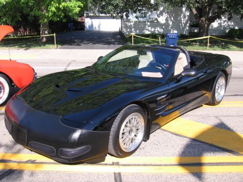 1989 Ford Mustang - A black convertible sports car is parked on a street with a red car beside it.