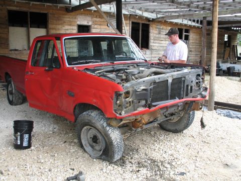 1995 Ford Bronco - A red pickup truck with its hood open and front end damaged sits on a gravel lot.