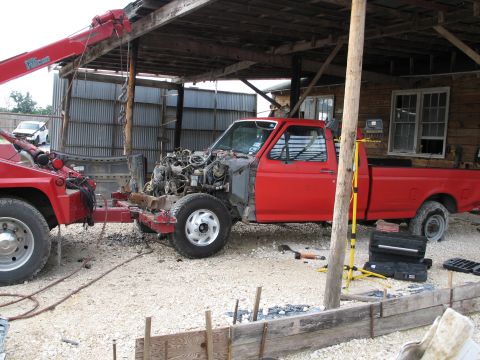 1995 Ford Bronco - A red pickup truck, missing its engine, is being towed by a red tow truck.