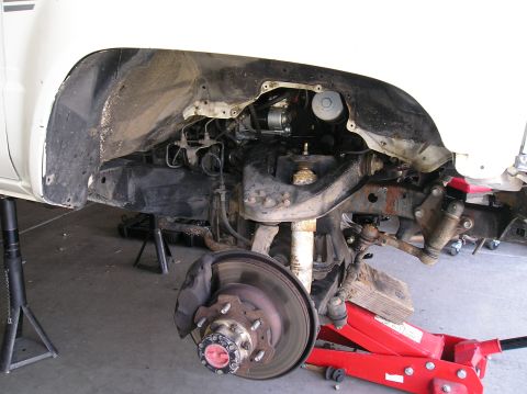 1986 Toyota Hilux - Front corner of a white truck with the fender and wheel removed, exposing the independent-front-suspension torsion bar setup, upper and low…