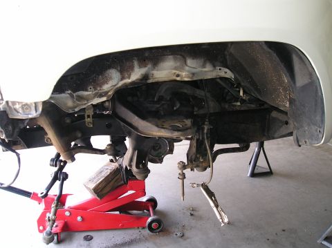 1986 Toyota Hilux - Front suspension components are disassembled and supported by a red hydraulic jack and jack stands, indicating repair or maintenance work.