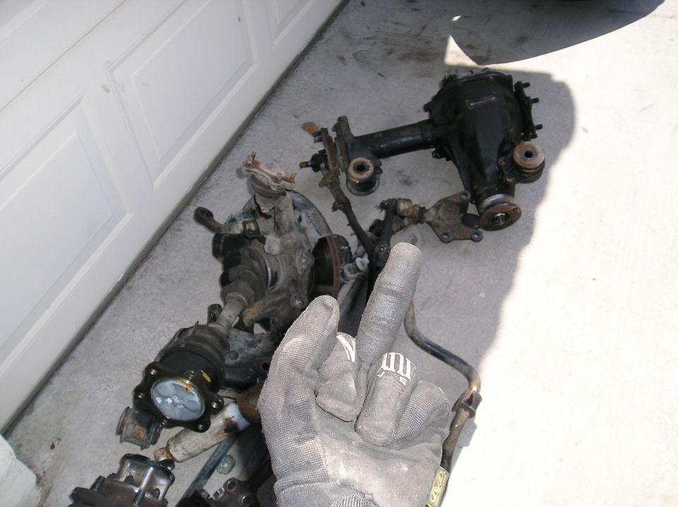 Pile of vehicle suspension components including a differential, CV axles, and control arms