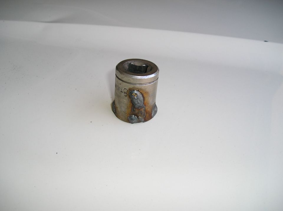 Metal socket with weld beads and heat discoloration on a white surface