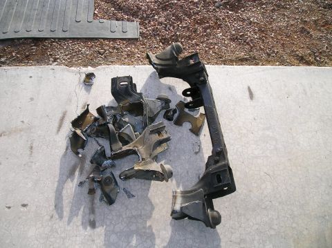1986 Toyota Hilux - A cut-apart steel front crossmember and a pile of torch-cut brackets and suspension mounts laid out on a concrete driveway, edges blackened…