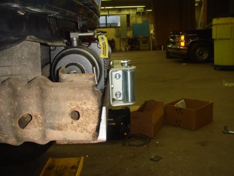 1996 Ford Bronco - A winch assembly is attached to the front of a vehicle frame in a workshop setting that appears to be a workshop.