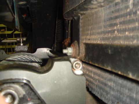 1996 Ford Bronco - Tight engine-bay shot of a radiator fin core, mounting bracket and a hex bolt with light surface rust.