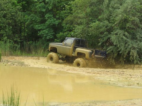 1976 Chevrolet Blazer - A lifted pickup truck navigates a muddy obstacle course, kicking up water and mud.