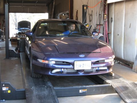 1996 Ford Probe - A man sits in a purple 1996 Ford Probe as it is positioned on a vehicle lift inside a workshop.