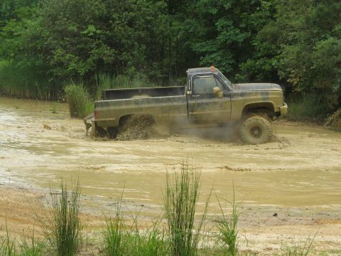 1976 Chevrolet Blazer - A muddy pickup truck navigates through a water-filled off-road course.