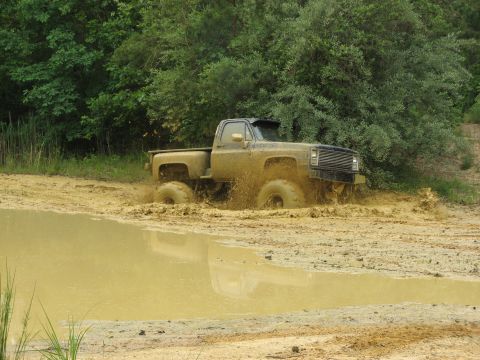 1976 Chevrolet Blazer - A pickup truck navigates through a muddy terrain, with trees lining the background.