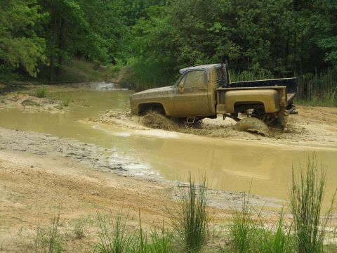 1976 Chevrolet Blazer - A muddy pickup truck navigates through a water and mud obstacle.