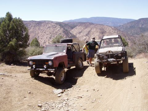 1967 Ford Bronco - A red 1967 Ford Bronco and another off-road vehicle are parked on a dusty mountain trail with people standing nearby.
