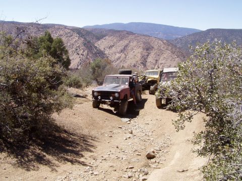 1967 Ford Bronco - A line of off-road SUVs, including a 1967 Ford Bronco, navigates a dusty mountain trail.