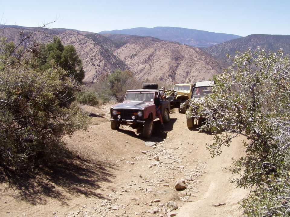 Red and black 1967 Ford Bronco on a dirt trail with two other SUVs behind it