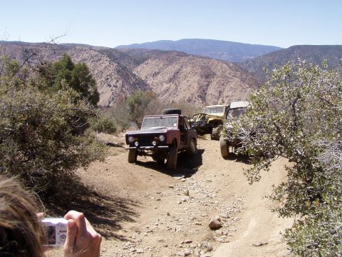 1967 Ford Bronco - A group of off-road vehicles navigates a steep, rocky trail in a mountainous, arid landscape.