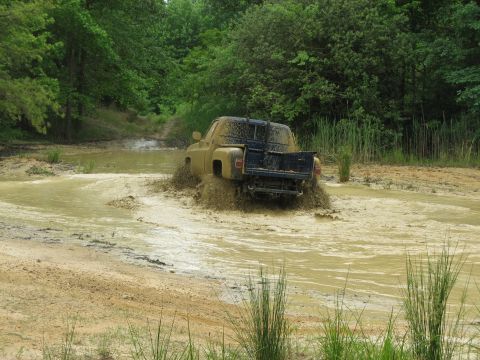 1976 Chevrolet Blazer - A tan pickup truck navigates a muddy trail, kicking up water and dirt.