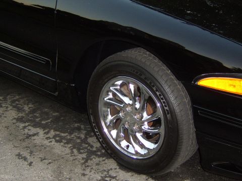 1996 Mercury Grand Marquis - Close-up of a black car's front wheel a chrome rim and an orange turn signal light.