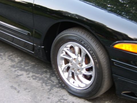 1996 Mercury Grand Marquis - Close-up of a black car's front wheel and fender area, showing chrome rims and an amber turn signal light.